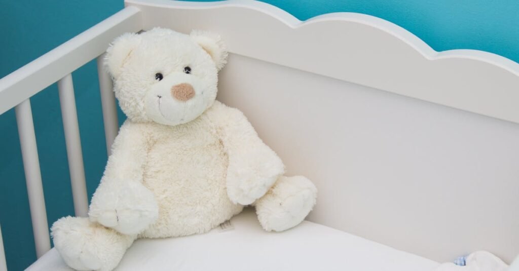 Soft teddy bear in a white crib against a vibrant blue wall, creating a comforting nursery atmosphere.