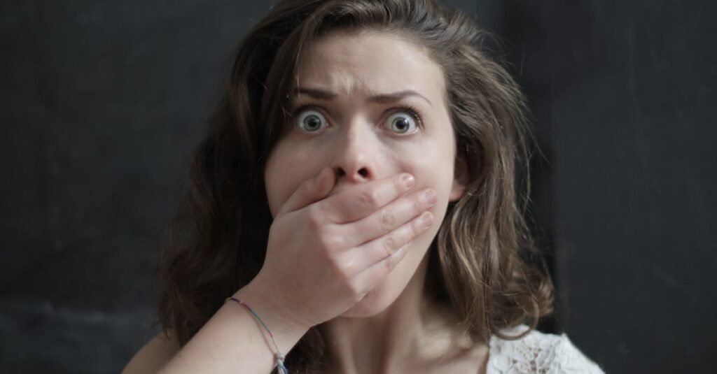 Close-up of a woman with a shocked expression, covering her mouth with her hand. Emotional and intense moment.
