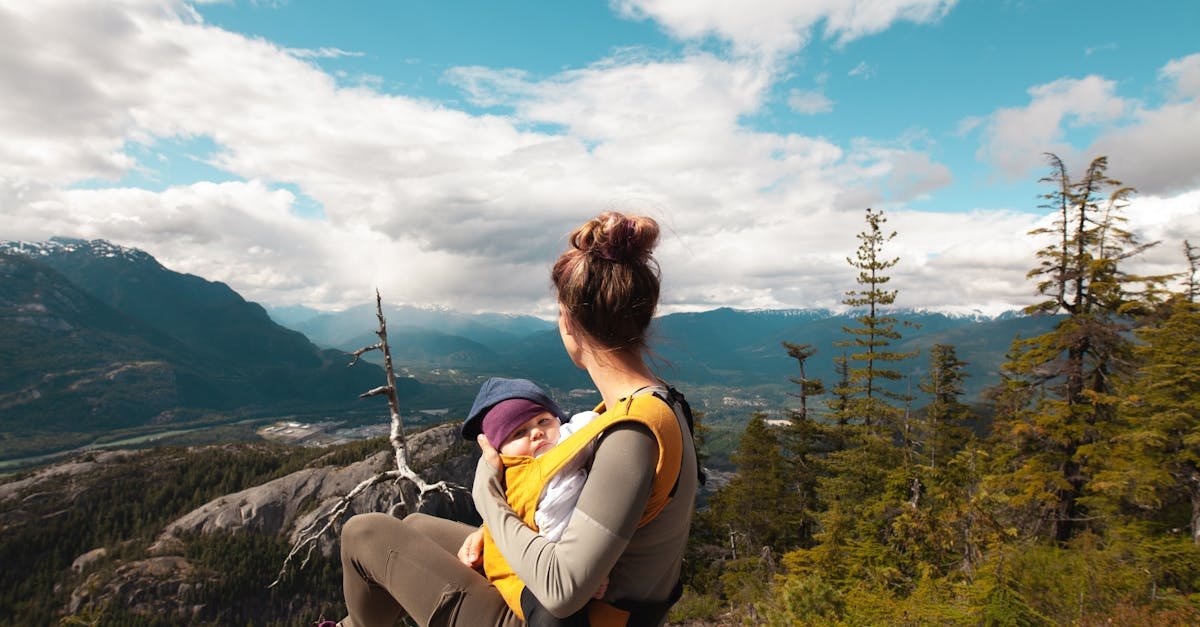 A mother sits with her baby overlooking a scenic mountain landscape, enjoying nature's beauty.